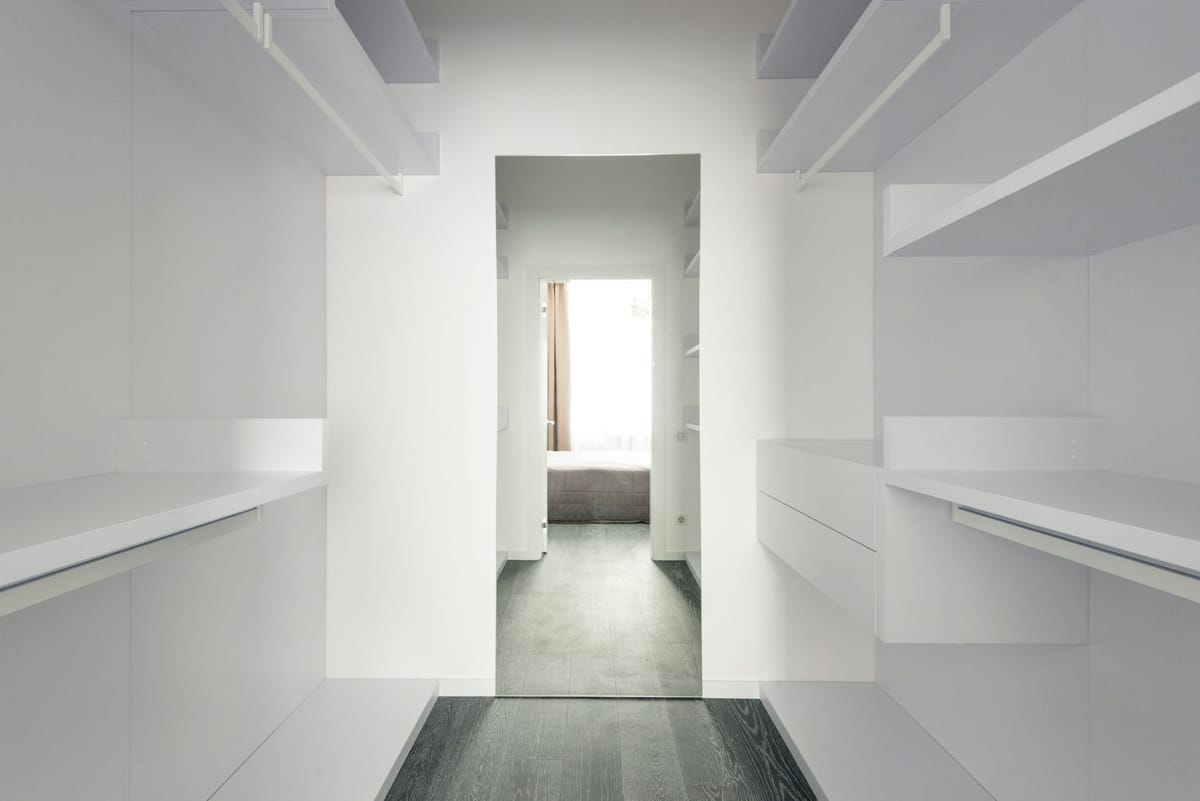A bright walk-in wardrobe with white shelving